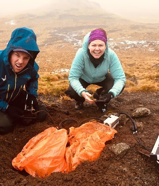 Two expeditioners squatting next to a solar panel in the field