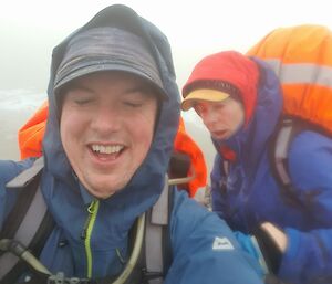 Two expeditioners with large backpacks being blown by the wind