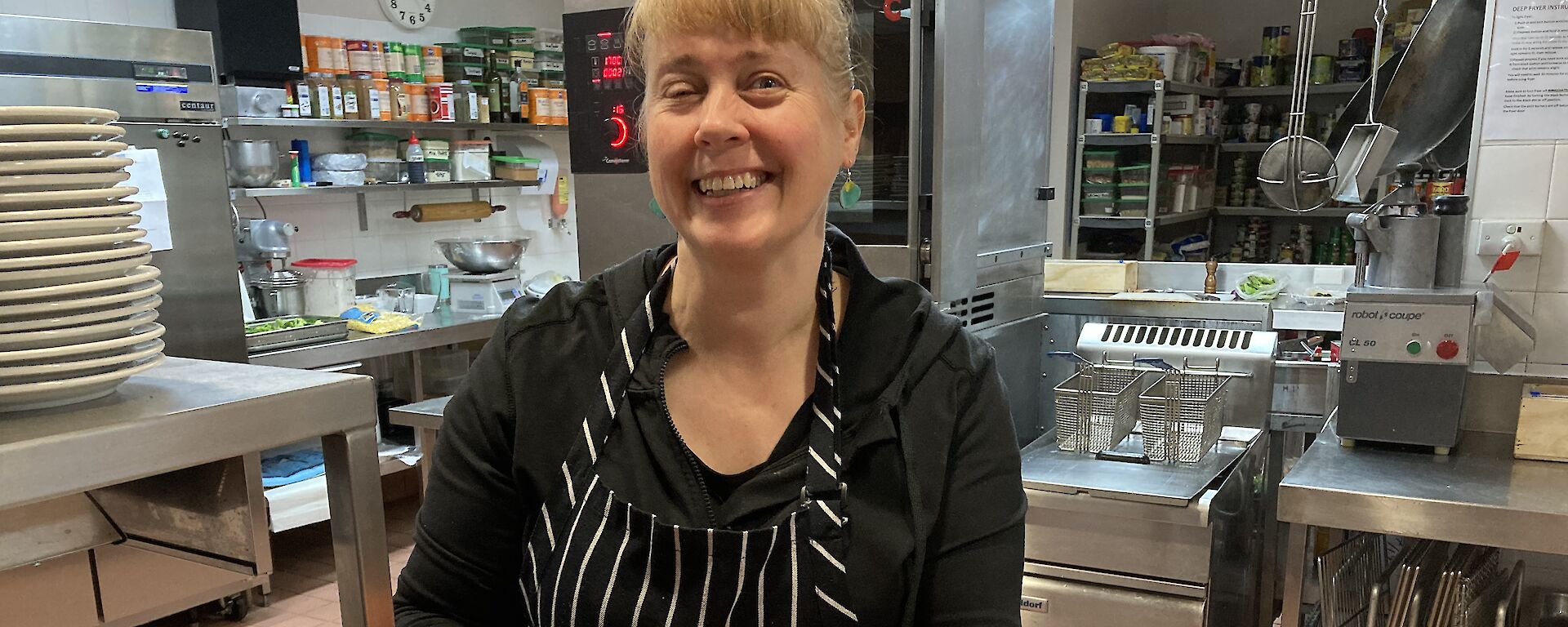 A lady in a chef apron holding a plate of Savoy biscuits with tomato on top
