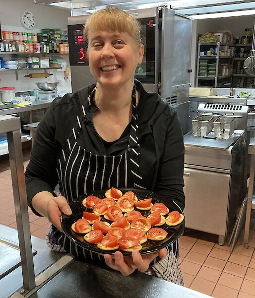 A lady in a chef apron holding a plate of Savoy biscuits with tomato on top