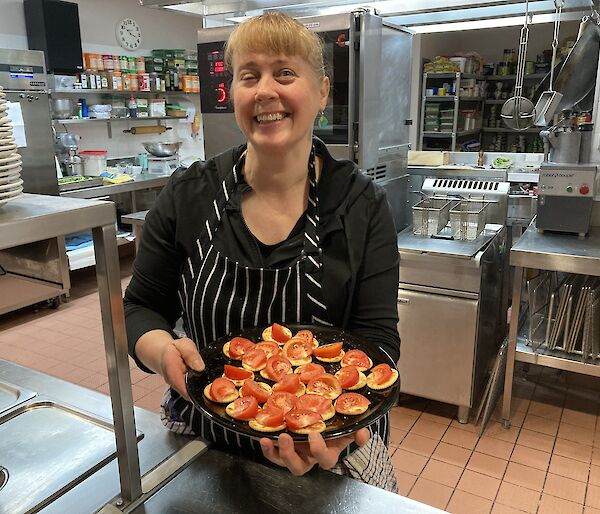 A lady in a chef apron holding a plate of Savoy biscuits with tomato on top