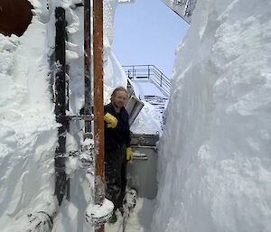 A man standing in a trench between a snow covered tank and a large snow drift smiling to camera