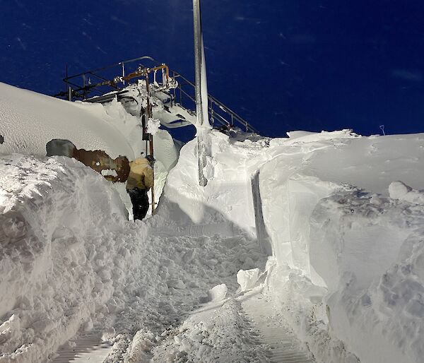 A large tanker covered in a snow drift with a man digging a trench towards it.