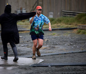 Two men outside dancing together.  One is wearing a Hawaiian shirt, the other is dressed as a penguin.