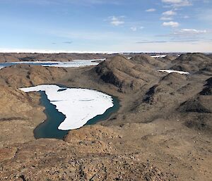 A shot looking down from a higher crag in to a rocky valley with an ice covered lake in the centre