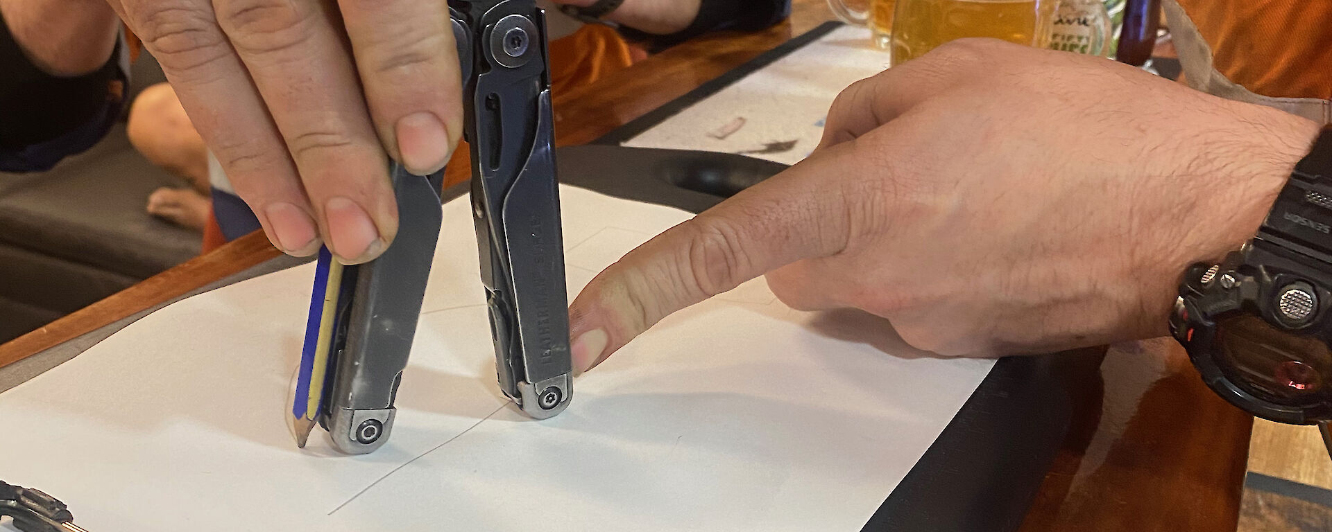 A man using a multi-tool to measure the distance on a piece of paper