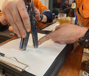 A man using a multi-tool to measure the distance on a piece of paper