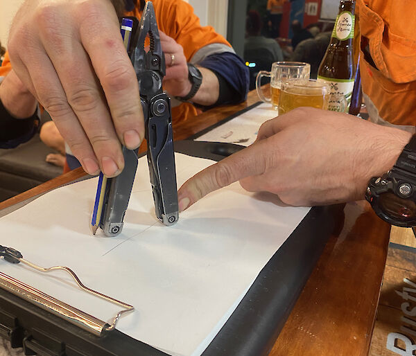 A man using a multi-tool to measure the distance on a piece of paper