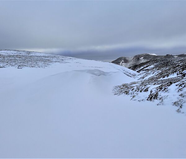 A  snowy landscape with a deep snowdrift of pristine snow at the centre