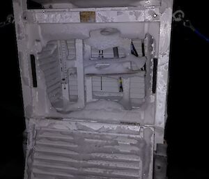A large metal box with the front open showing equipment inside all covered in snow.