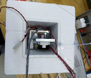 A polystyrene box sitting on a bench, with electric equipment in the centre with wires coming out.