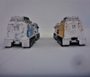 The back of the yellow and blue Hagglund vehicles all covered in snow.