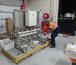 A man in hi vis works on a heating system in a warehouse