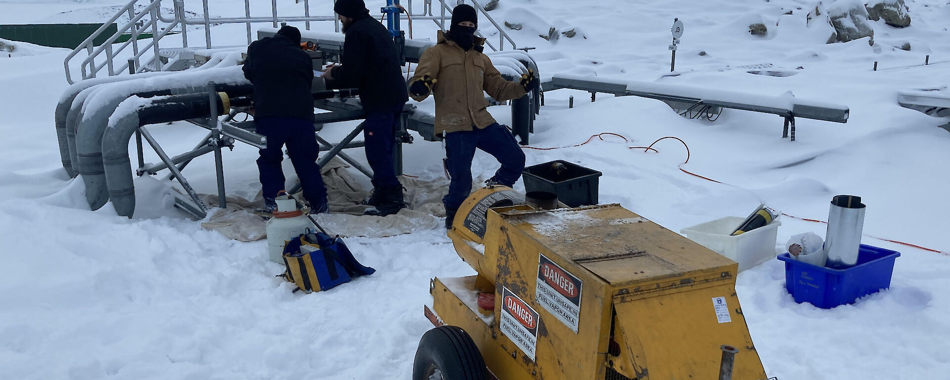 Three men in deep snow with a mobile generator fixing a burst pipe