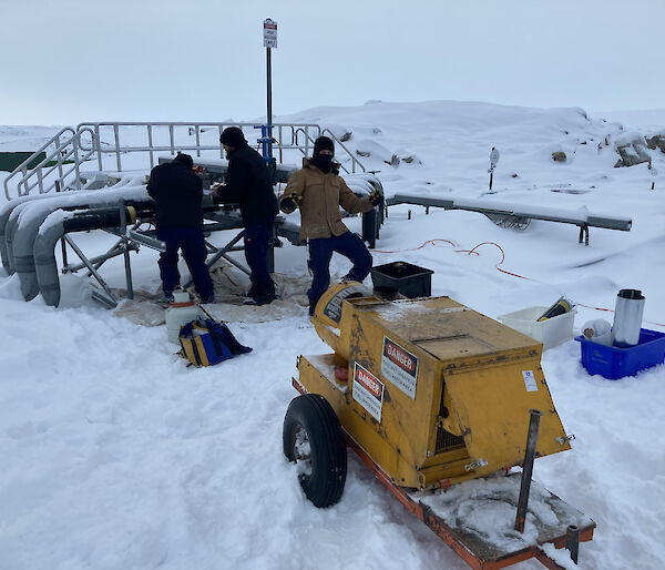 Three men in deep snow with a mobile generator fixing a burst pipe
