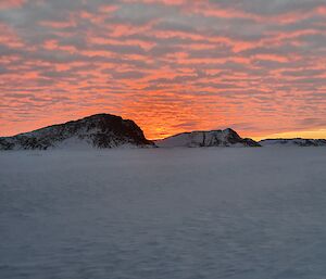 An icy landscape with rocky hills on the horizon and an orange sky behind