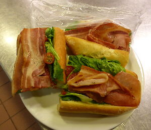 Three BLT rolls on a plate with fresh green salad and fresh tomatoes grown in our hydroponics facility.