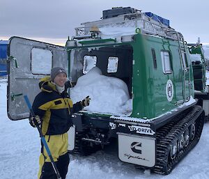 A man stands next to a green Hagglund in a snowy landscape with snow in the back.  He is smiling to camera.