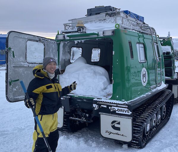 A man stands next to a green Hagglund in a snowy landscape with snow in the back. He is smiling to camera.