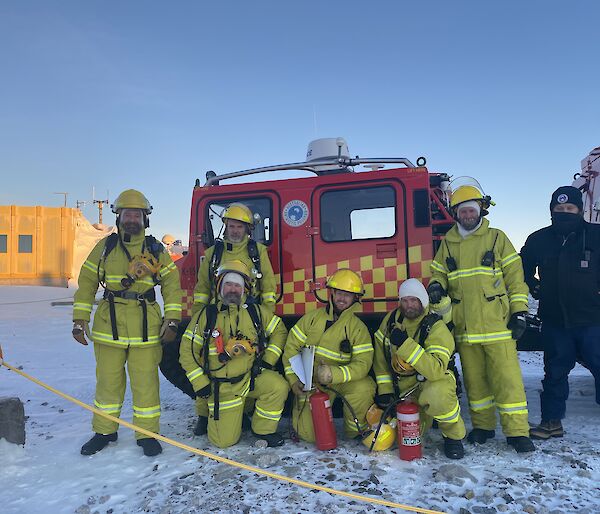 A group photo of people in fire safety gear and helmets in front of a red emergency Hagglund