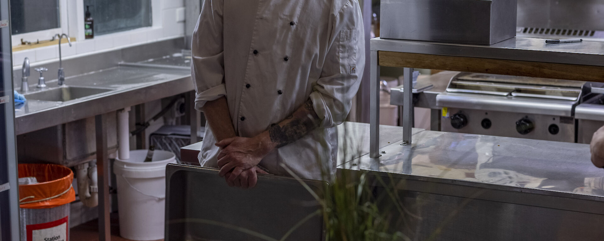 A chef in whites standing behind a decorated table set in front of a commercial kitchen, smiling to camera