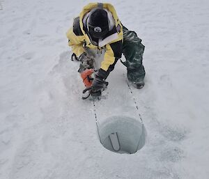 A man works a chainsaw to cut the sea ice