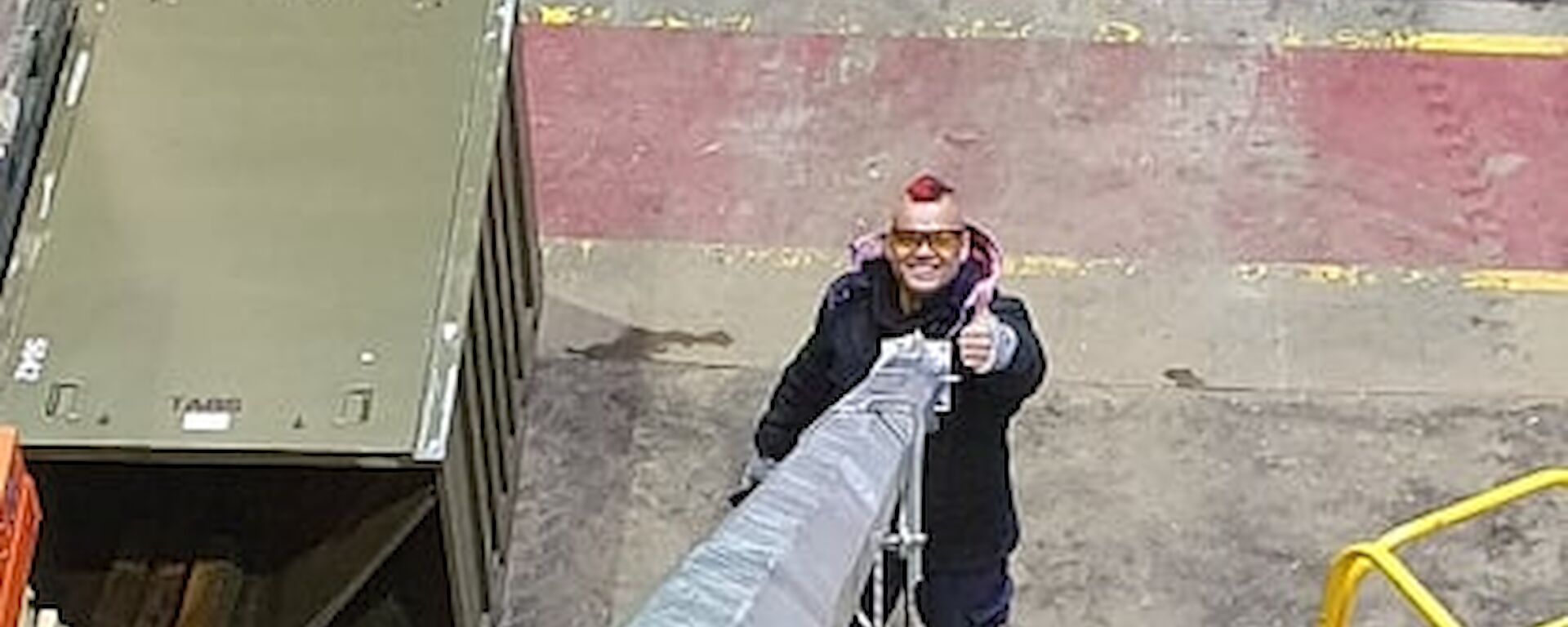 A image taken down the shaft of a large metal pipe.  A man stands at the bottom holding the pipe with one thumbs up.