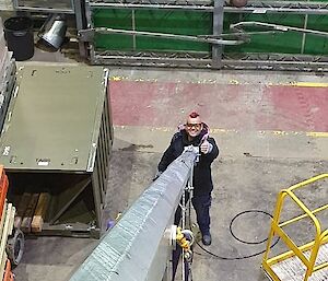 A image taken down the shaft of a large metal pipe.  A man stands at the bottom holding the pipe with one thumbs up.