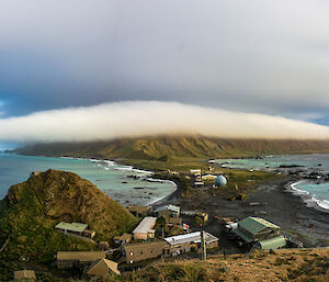 Looking down from one hill, across an isthmus to the green hills on the other side.  Low cloud hangs over the hills.