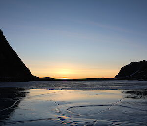 Sun setting in the distance with mirror like ice in the foreground.