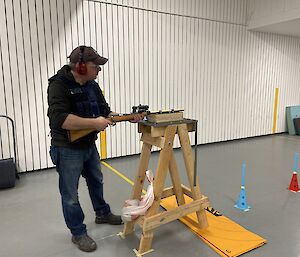 A man stands holding a dart gun positioned on a timber support