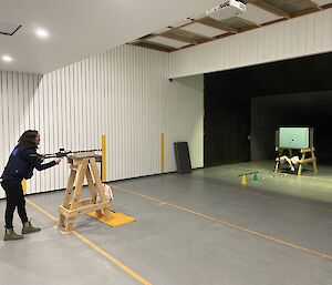 A woman standing behind a dart gun taking aim at a board in the distance.