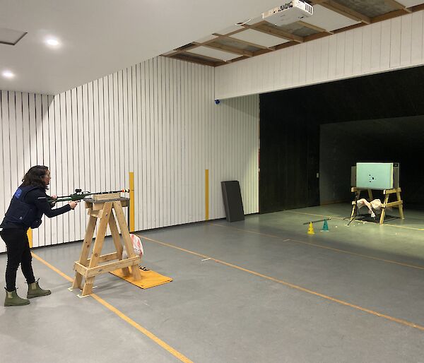 A woman standing behind a dart gun taking aim at a board in the distance.