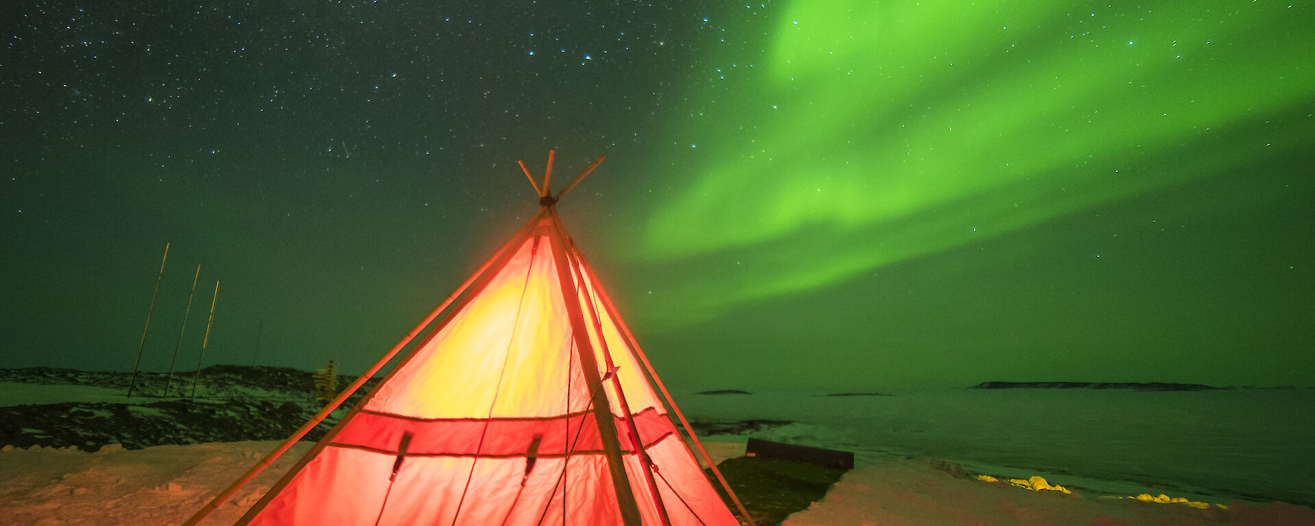 A red polar tent lit from within against a green aurora in the sky