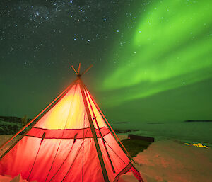 A red polar tent lit from within against a green aurora in the sky