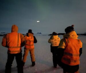 Four people with backs to the camera, looking at some approaching lights in the sky