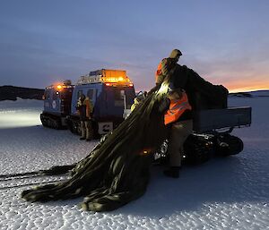 Two men pull a parachute of the ice in to a trailer attached to the back of a Hagglund.