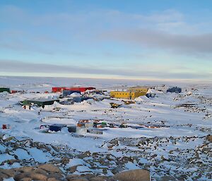 A view across a ice covered rocky landscape towards the colourful buildings of Casey station.