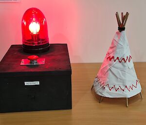 A home made black box with a red light and push button on top.  A sticker on the box says 'internet' .  Beside it is a homemade miniature wigwam.