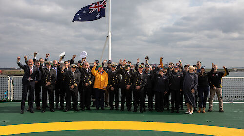 A large group of people standing on the deck of a ship underneath a flagpole with the Australian flag