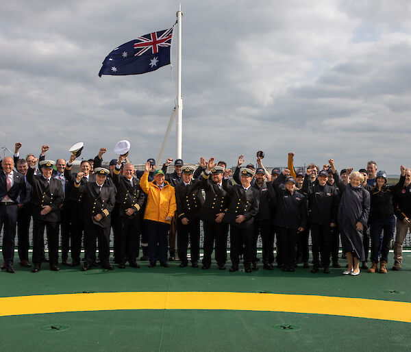 A large group of people standing on the deck of a ship underneath a flagpole with the Australian flag