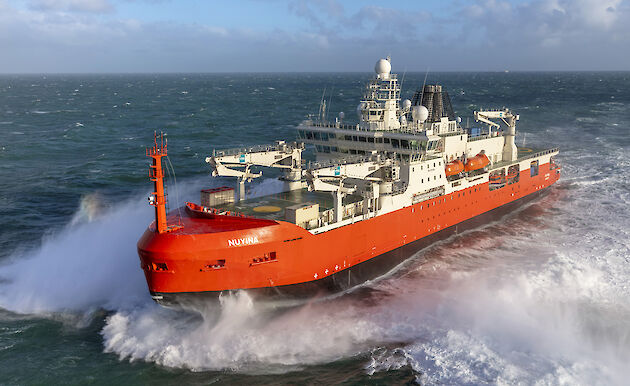 A large red research vessel plowing through the waves