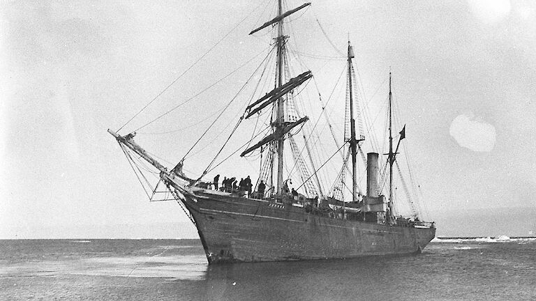 Black and white photo of a wooden ship in Antarctica in the early 1900s.