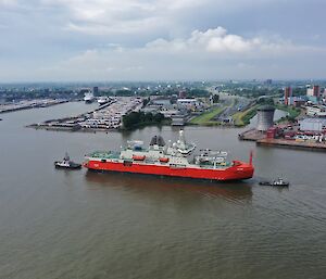 New icebreaking ship Nuyina being escorted by two tugs near a busy port in the Netherlands.