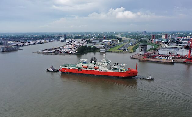 New icebreaking ship Nuyina being escorted by two tugs near a busy port in the Netherlands.