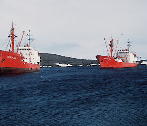 Two red and white icebreaking ships anchored on the Antarctic coast.