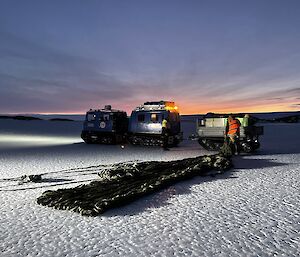 A parachute laying on the sea ice ready to be loaded into the trailer on the blue Hagglund.