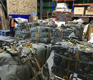 A large warehouse full of unopened air drop pallets.  A man in hi-vis stands beside one of the pallets.