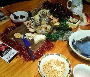 A table with a cheese platter decorated with tinsel, a block of chocolate and other nibbles.