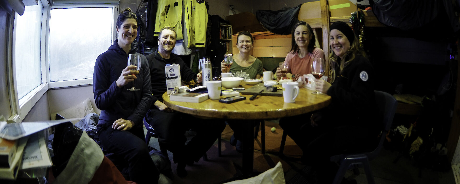 A group of people round a table, smiling to camera and holding up their glasses.